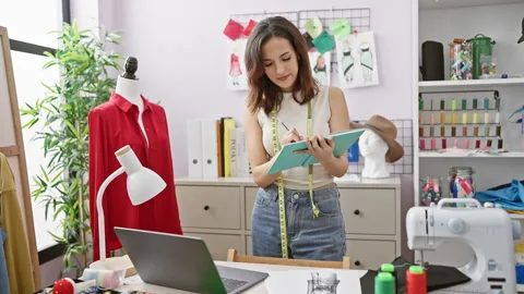 Hispanic woman taking notes in tailor shop, surrounded by colorful threads,.. Stock Footage 266484531