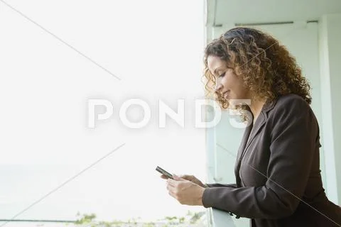 Hispanic Woman Text Messaging On Balcony
