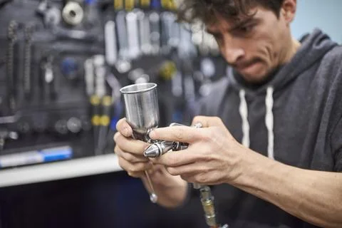 Hispanic worker preparing a spray paint gun in his bike workshop Stock Photos