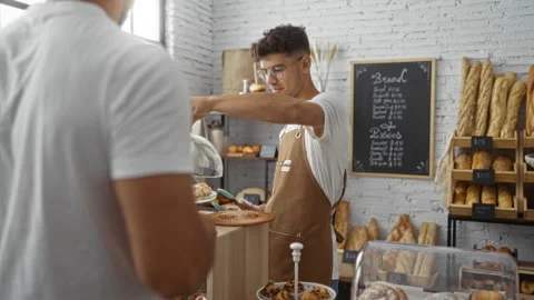 Hispanic worker smiling while serving a male customer in a bakery with an a.. Video stock 294635805