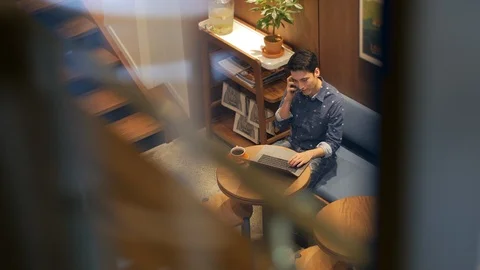 Hispanic young man sitting in coffee shop with laptop talking on cell phone Vídeo Stock 101659483