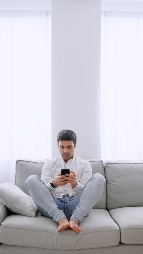 Hispanic young man using phone on sofa Stock Footage 262491183