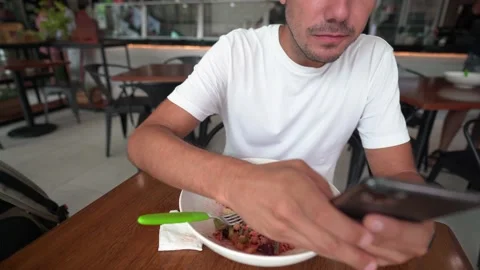 Hispanic young man writes a message on his smart phone while eating salad Stock Footage 164592711
