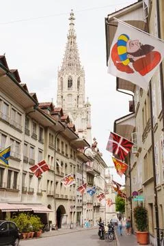 Historic Bern street lined with flags, medieval facades, cathedral spire and Stock Photos