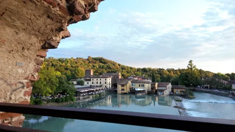 Historic brick arch frames a riverside village with old buildings and lush Stock Footage 297240740
