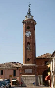 Historic brick clock tower with a religious statue and bells in comacchio Stock Photos