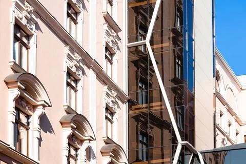 A historic building with decorative elements stands beside a contemporary str Stock Photos