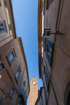 Historic Clock Tower Framed by Old Town Buildings and Clear Blue Sky, Orvie.. Stock Photos