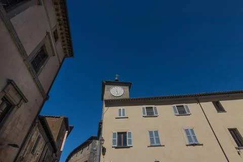 Historic Clock Tower Framed by Old Town Buildings and Clear Blue Sky, Orvie.. Stock Photos