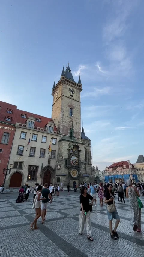 Historic clock tower over cobblestone plaza with pedestrians pausing and, with Видео 344585204
