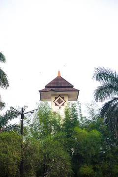 Historic clock tower standing tall amidst lush green trees under overcast sky Stock Photos