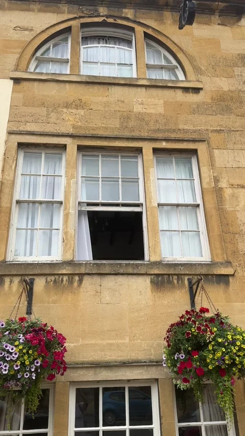 Historic Cotswold Stone Building Facade with Arched Window and Hanging Baskets 库存影片 342633241