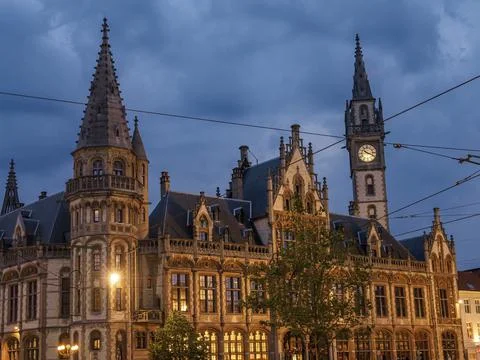 Historic gothic building with clock tower and illuminated street lamps at dusk, Stock Photos