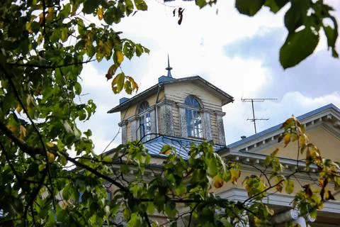 Historic manor house tower framed by green tree branches under cloudy sky Foto stock