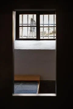 Historic prison cell interior viewed through doorway with barred window and bed Foto stock