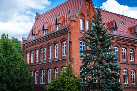 Historic Red Brick Building Surrounded by Lush Green Trees on a Cloudy Day Stock Photos