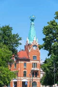 Historic red brick clock tower against blue sky with trees. House under the.. Stock Photos
