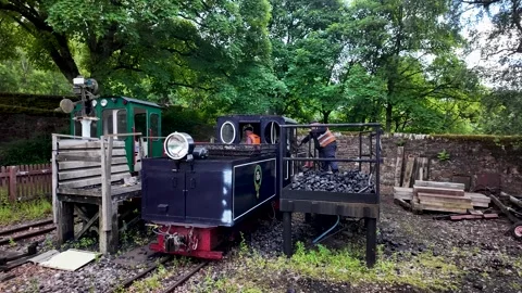 Historic steam engine with an engineer inside the cabin departing from the Stock Footage 339414909