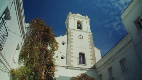 A historic white bell tower with a clock stands against a bright blue sky Stock Footage 299910932