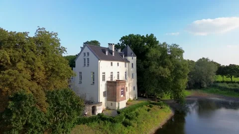 Historic white castle surrounded by lush green forest, located near a calm Stock Footage 315520105