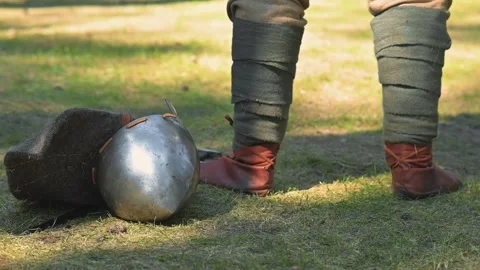 Historical props on a grassy area during daylight. One person wears brown Vidéo 345036636