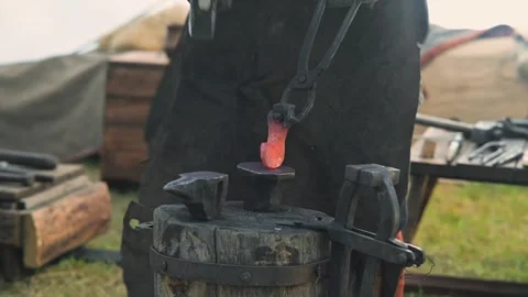 In a historical reenactment, a blacksmith works at an anvil, heating metal in a Stockbeeldmateriaal 345032649