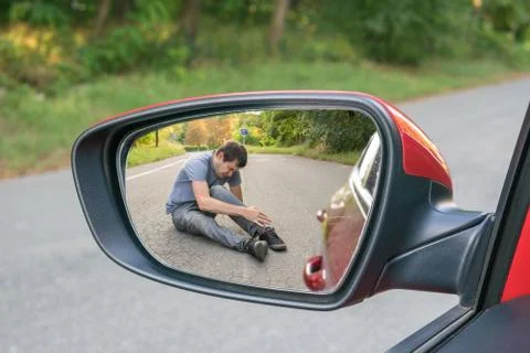 Hit and run concept. View on injured man on road in rear mirror of a car. Stock Photos