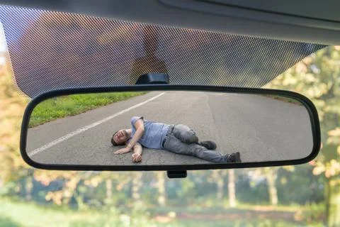 Hit and run concept. View on injured man on road in rear mirror of a car. Stock Photos