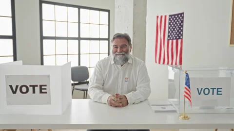 Hoary bearded man points finger to camera at polling table with ballot box .. Stock Footage 339200806