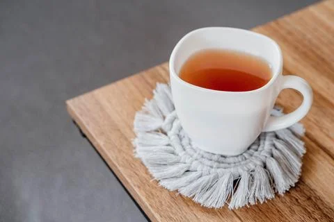 Hobby handmade macrame. Tea in a cup on a gray macrame stand on a wooden tabl Fotos de archivo