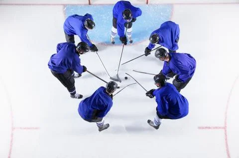 Hockey players in blue uniforms huddling around puck on ice Stock Photos