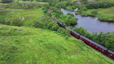 Hogwarts Express train is traveling down a track through a grassy field Stock Footage 306560638