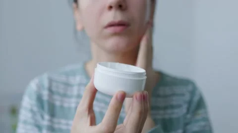 Hold hand jar of face cream woman gently applies cream to her face to nourish Stock Footage 227734591