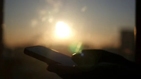 Hold the phone in his hand on a background of sunset, with glare from the sun Stock Footage 72177573