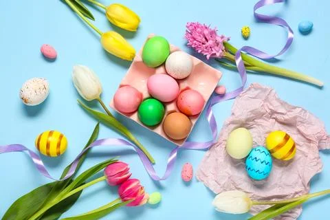 Holder with painted Easter eggs, flowers and ribbon on blue background Stock Photos