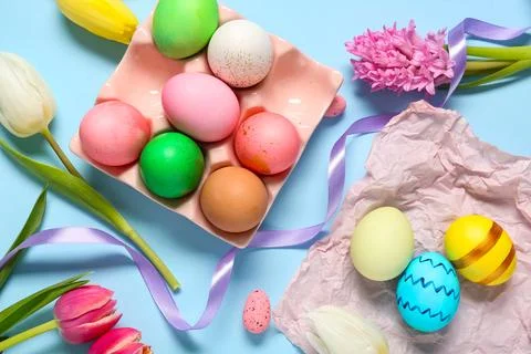 Holder with painted Easter eggs, flowers and ribbon on blue background Stock Photos