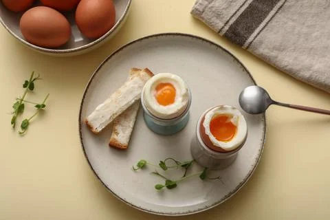 Holders with soft boiled eggs, micro green and pieces of bread on light backg Stock Photos