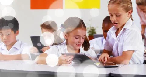 Holding and tapping tablets, two students wearing white shirts interacting at 스톡 사진