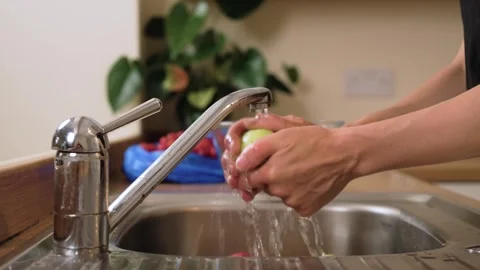 Holding apple under faucet preparing homemade compote. Cleaning juicy fruit with Видео 331207388