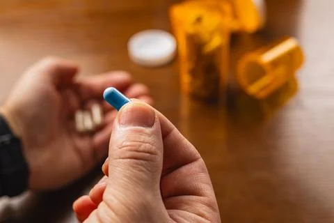Holding a blue capsule while sitting near medicine containers on a table Foto stock