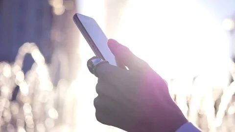 Holding a cell phone, flipping the screen, on a background of a fountain in the Stock Footage 76340357