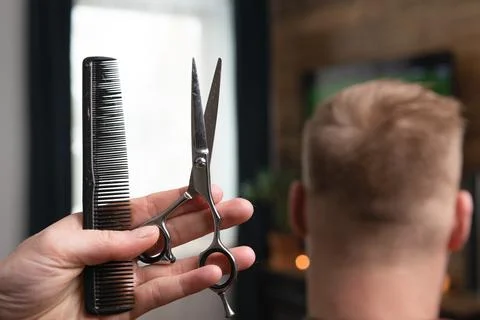 Holding comb and scissors in front. Cutting husband's hair at home in front o Stock Photos