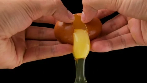 Holding a cracked egg. Black background. Breaking an egg. Slow motion. Stock Footage 144655673