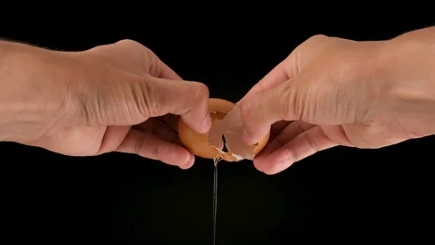 Holding a cracked egg. Breaking an egg .Black background. Slow motion. Stock Footage 144655366