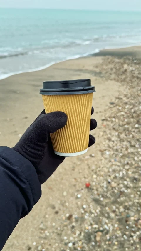 Holding a cup of coffee on a beach during a cloudy day by the water Stock Footage 341397006