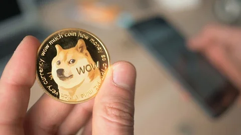 Holding a Dogecoin Cryptocurrency in Hand and a Smartphone Device Stock Footage 87769059