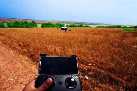 Holding a drone controller and flying by the drone on a field next to a river Stock Photos
