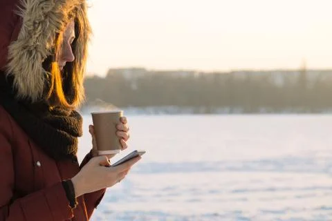 Holding hot drink and using smartphone outdoors in winter