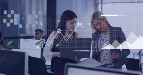 Holding laptop, pointing at documents, two women in blazer jacket reviewing data Stock Photos