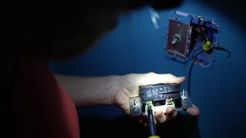 Holding the light switch in her hand, a woman screw the electrical wires onto Vídeo Stock 277709997